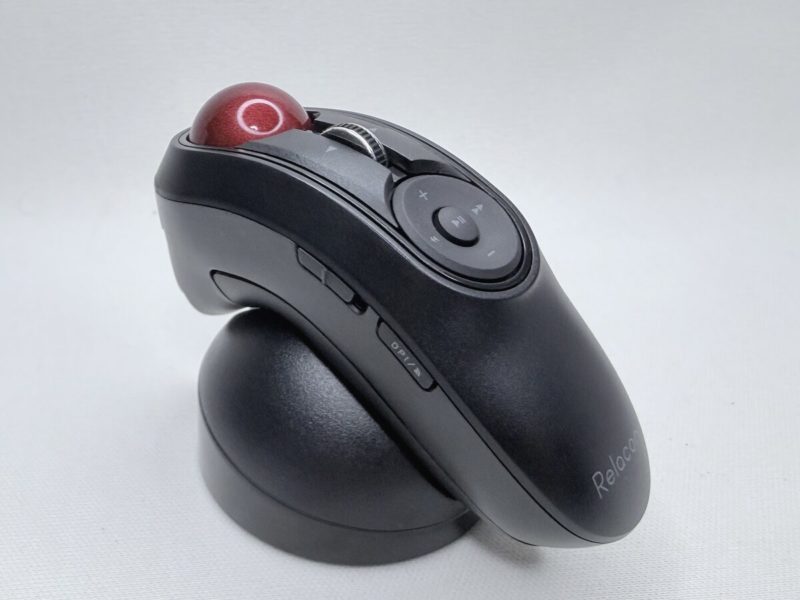 白い布の上に置かれた、黒い握り型のトラックボール。上面の手前に赤い球、その奥に丸いメディア操作のボタンが並び、本体はドーム型の黒いスタンドに立てかけてある