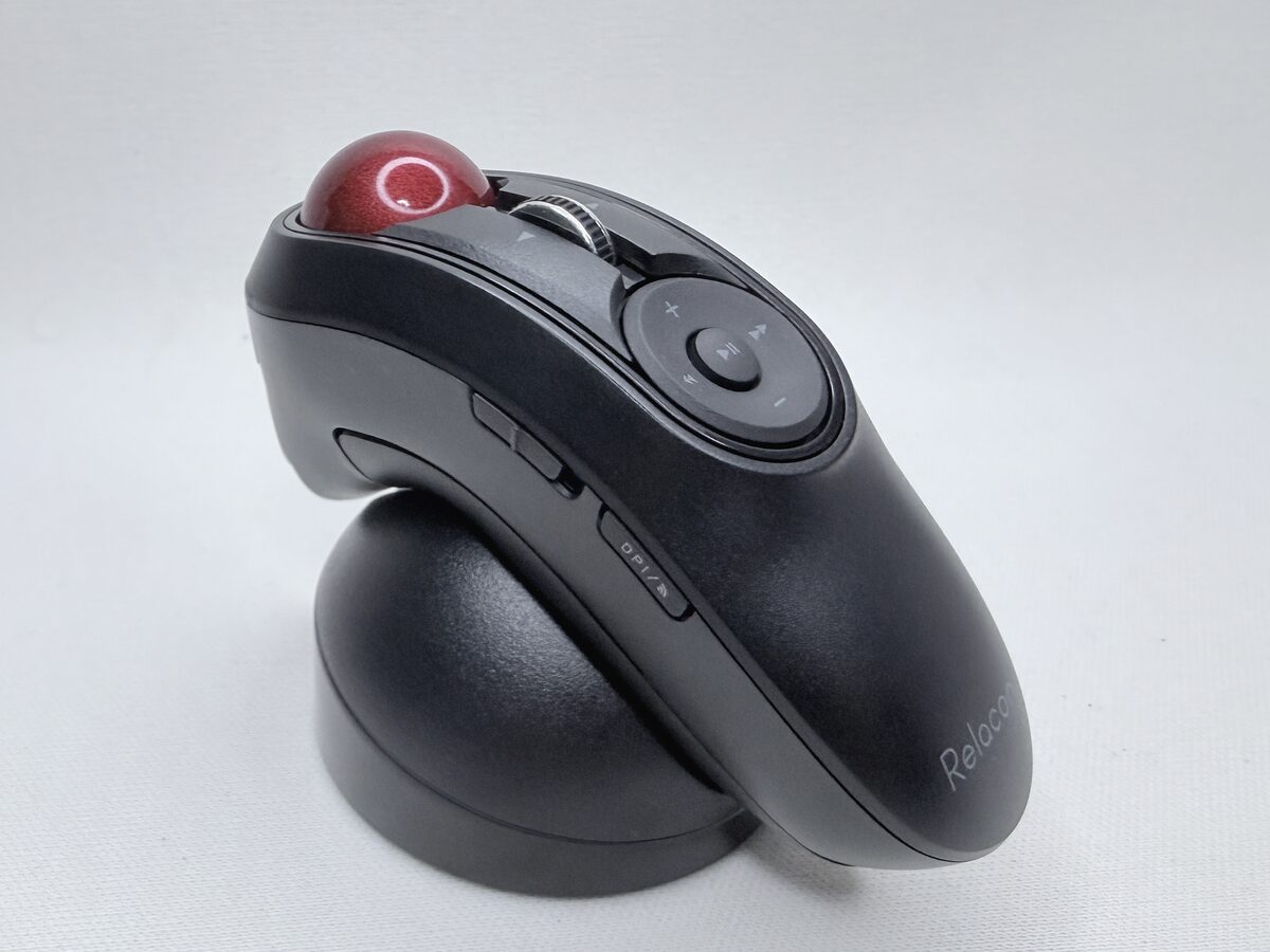 白い布の上に置かれた、黒い握り型のトラックボール。上面の手前に赤い球、その奥に丸いメディア操作のボタンが並び、本体はドーム型の黒いスタンドに立てかけてある