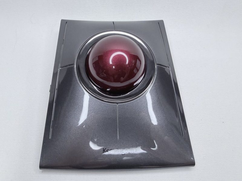白い布の上に置かれた、黒みがかった銀色の四角いトラックボール。中央に大きな赤紫の球があり、球のまわりの縁はまだ黒く、傷んでいない